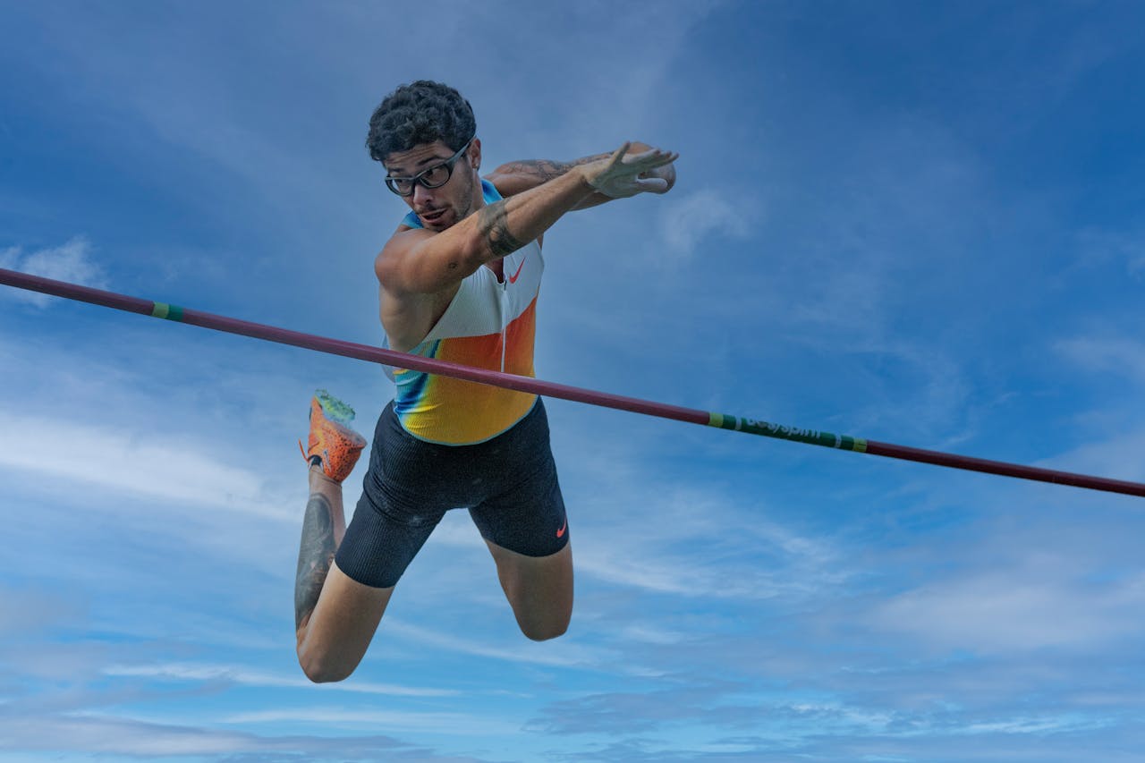 Athlete soaring over the bar during a pole vault with a bright blue sky background.
